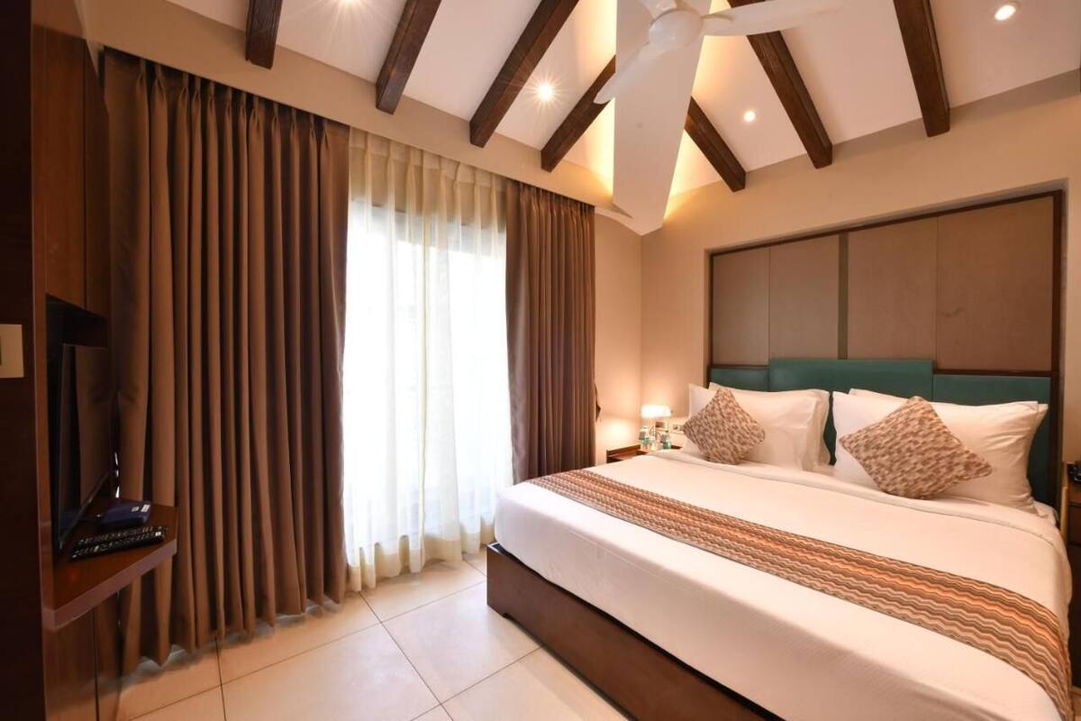 Una habitación de hotel con una cama grande, cortinas, un ventilador de techo y una televisión.