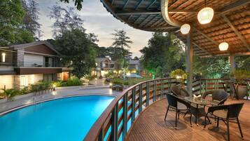 A swimming pool with a wooden deck, outdoor furniture, and a covered area with hanging lights.