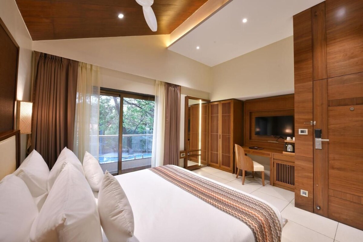 A hotel room with a large bed, a desk with a chair, a television, and a wardrobe.