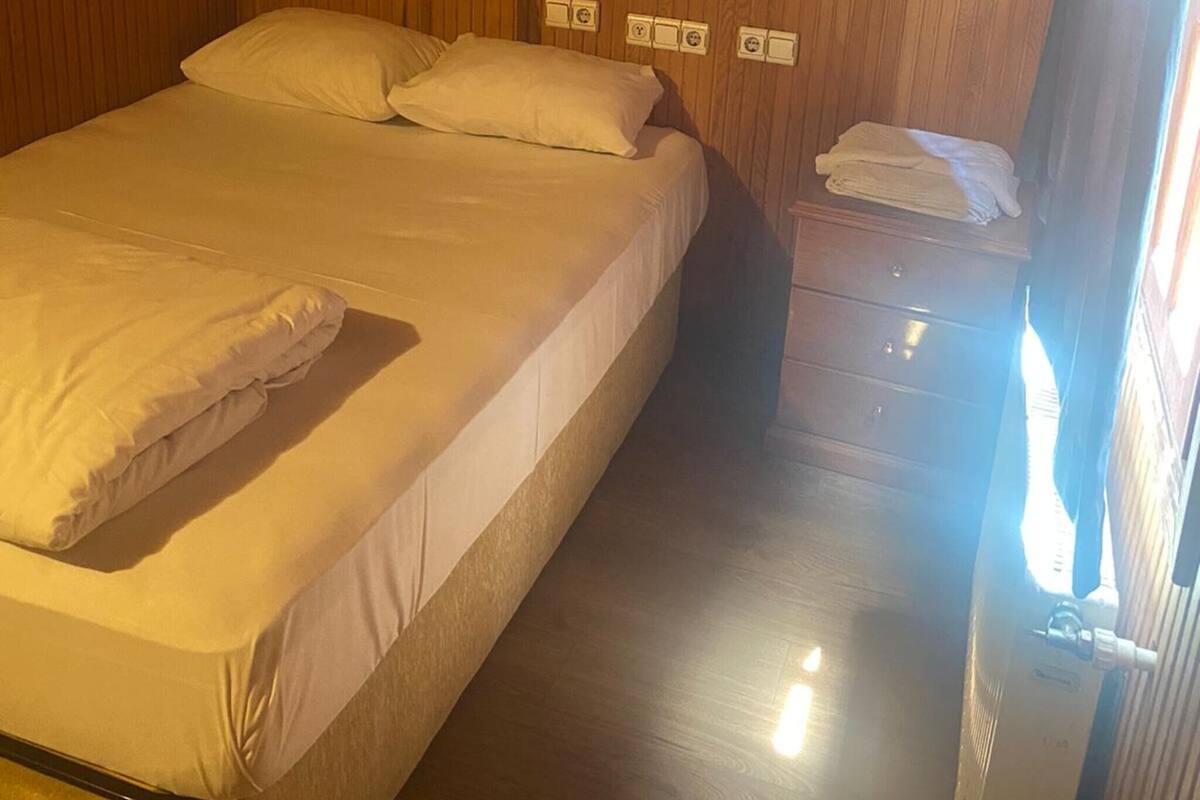 A wooden-paneled room with a bed, bedside table, and wall-mounted light fixtures.