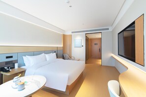 Hotellihuone, jossa on sänky, yöpöytä, tuoli, televisio ja työpöytä tuolilla.