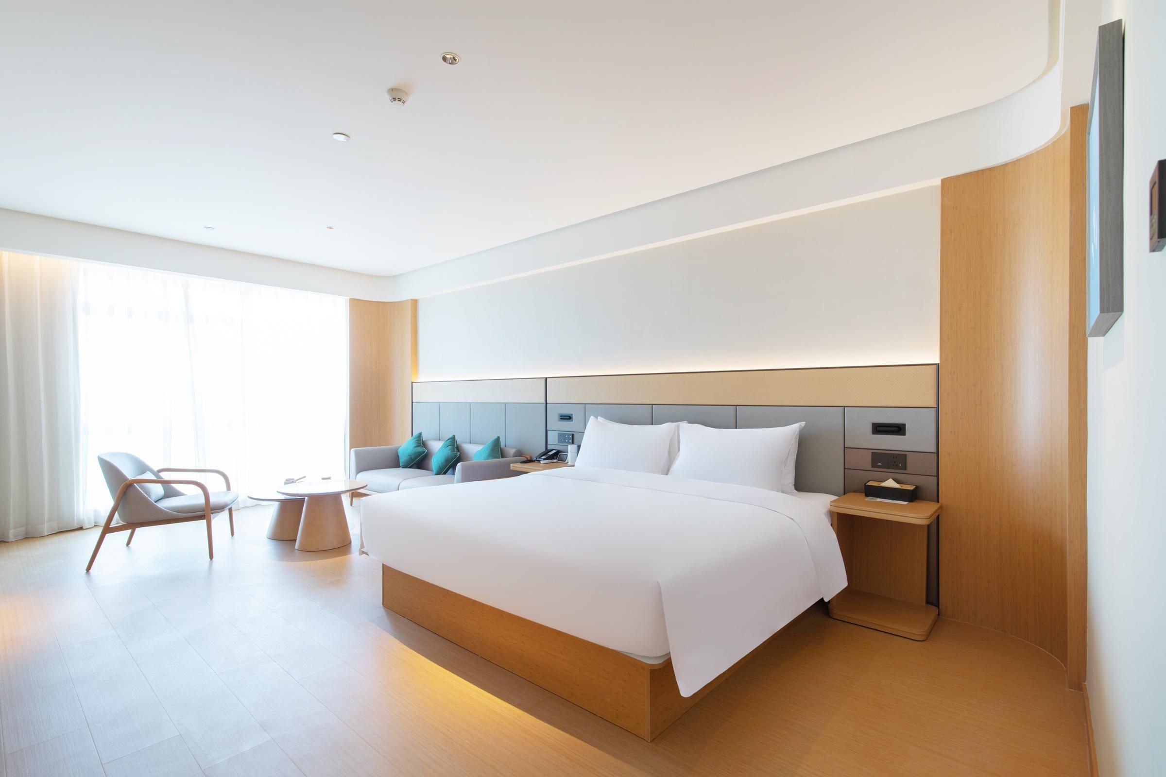 A modern hotel room with a large bed, bedside tables, a chair, and a small table.