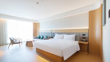 A modern hotel room with a large bed, bedside tables, a chair, and a small table.
