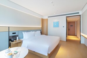 A modern hotel room with a large bed, bedside table, and a small round table with a cup and a book. - Ji Hotel Hefei Huaxia International Tea Expo City (Hefei)