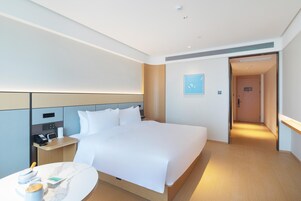 Quarto de hotel moderno com uma cama grande, mesa de cabeceira e uma pequena mesa redonda com uma chávena e um livro.