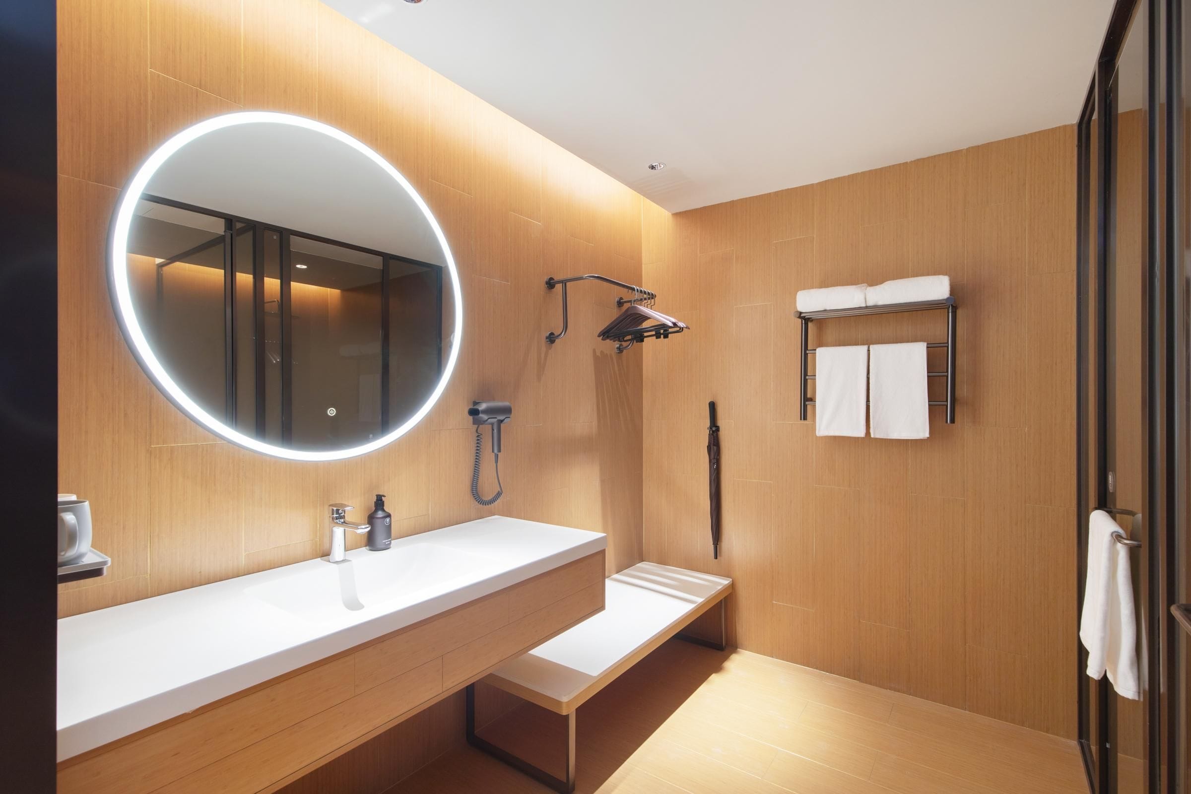 Un baño moderno con un espejo grande, un lavabo, una ducha y un perchero para toallas.