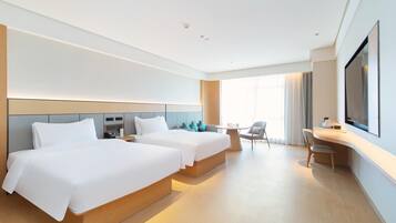 Una habitación de hotel moderna con dos camas, un escritorio, una silla y un televisor grande.
