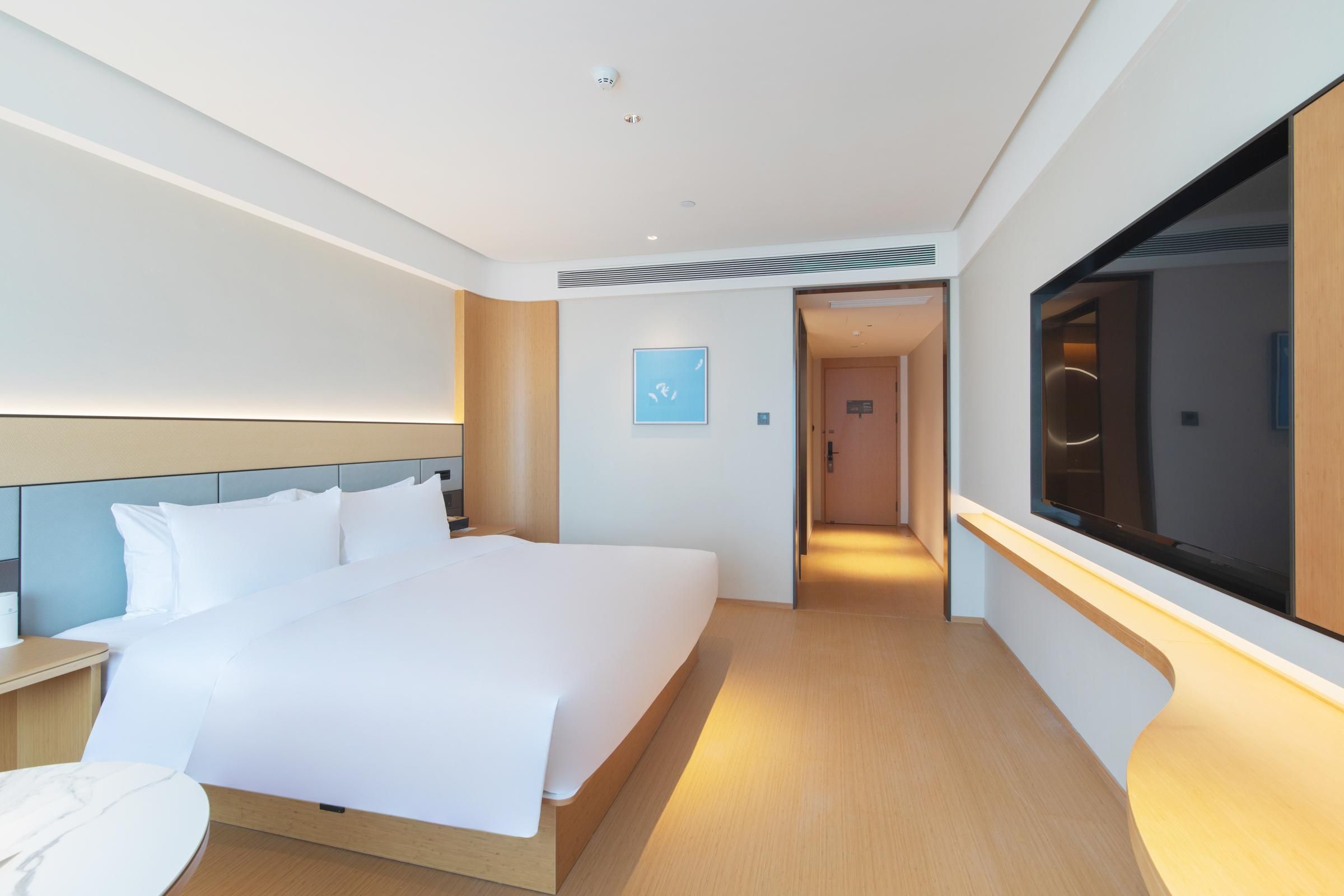 Una habitación de hotel moderna con una cama grande, mesitas de noche, un televisor y un pasillo que conduce a otra habitación.