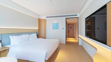 Una habitación de hotel moderna con una cama grande, mesitas de noche, un televisor y un pasillo que conduce a otra habitación.