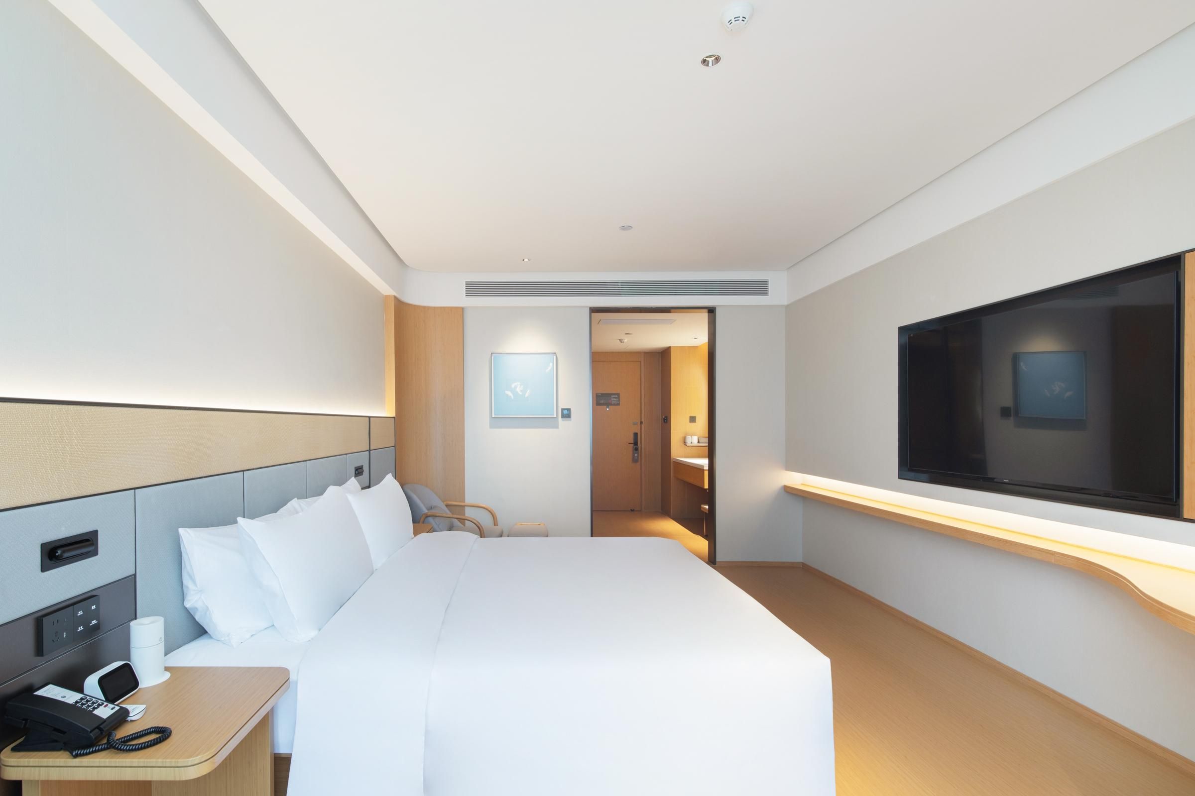 A hotel room with a bed, bedside table, phone, TV, and a door leading to a bathroom.