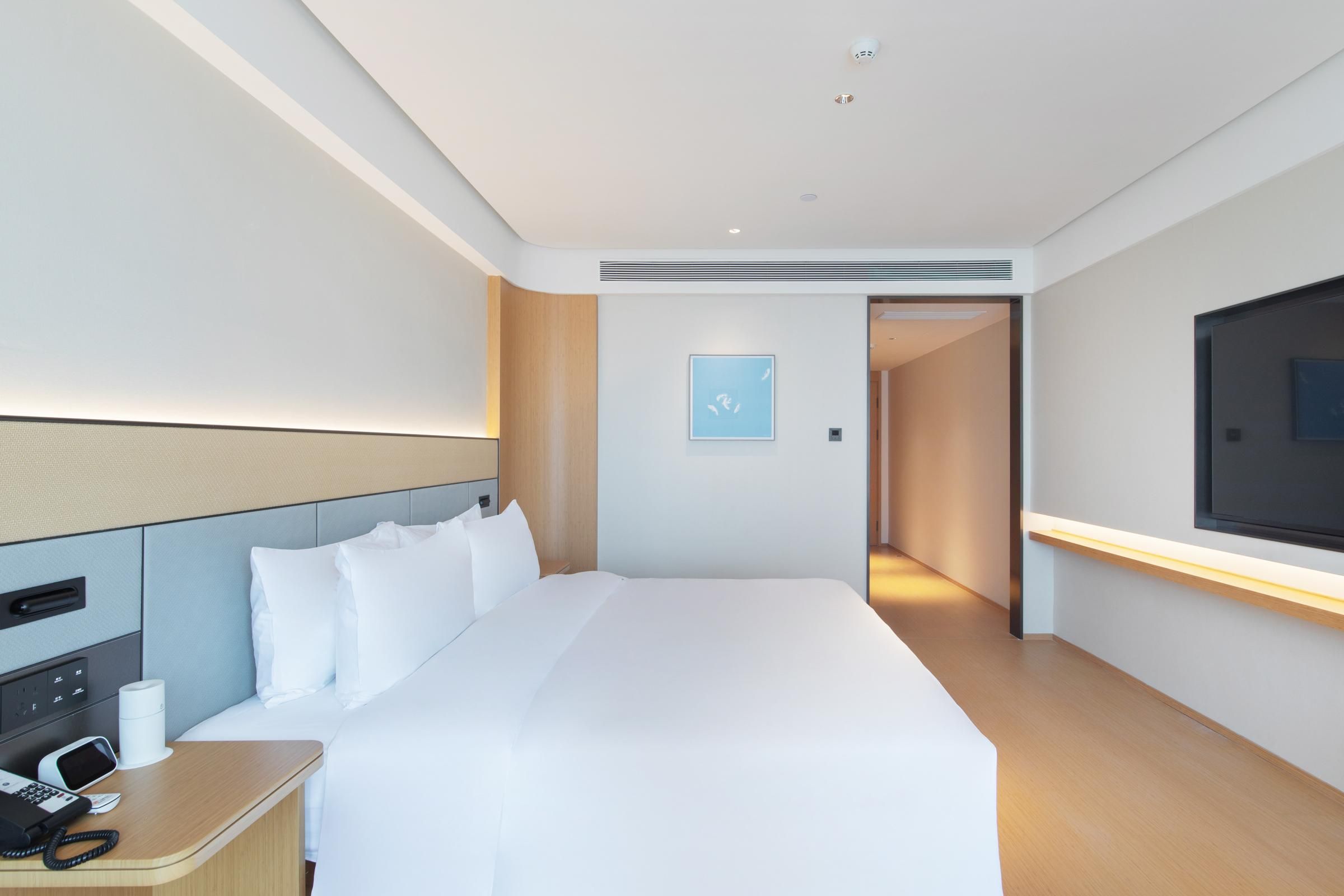 A modern hotel room with a large bed, bedside table with a phone, and a TV mounted on the wall.