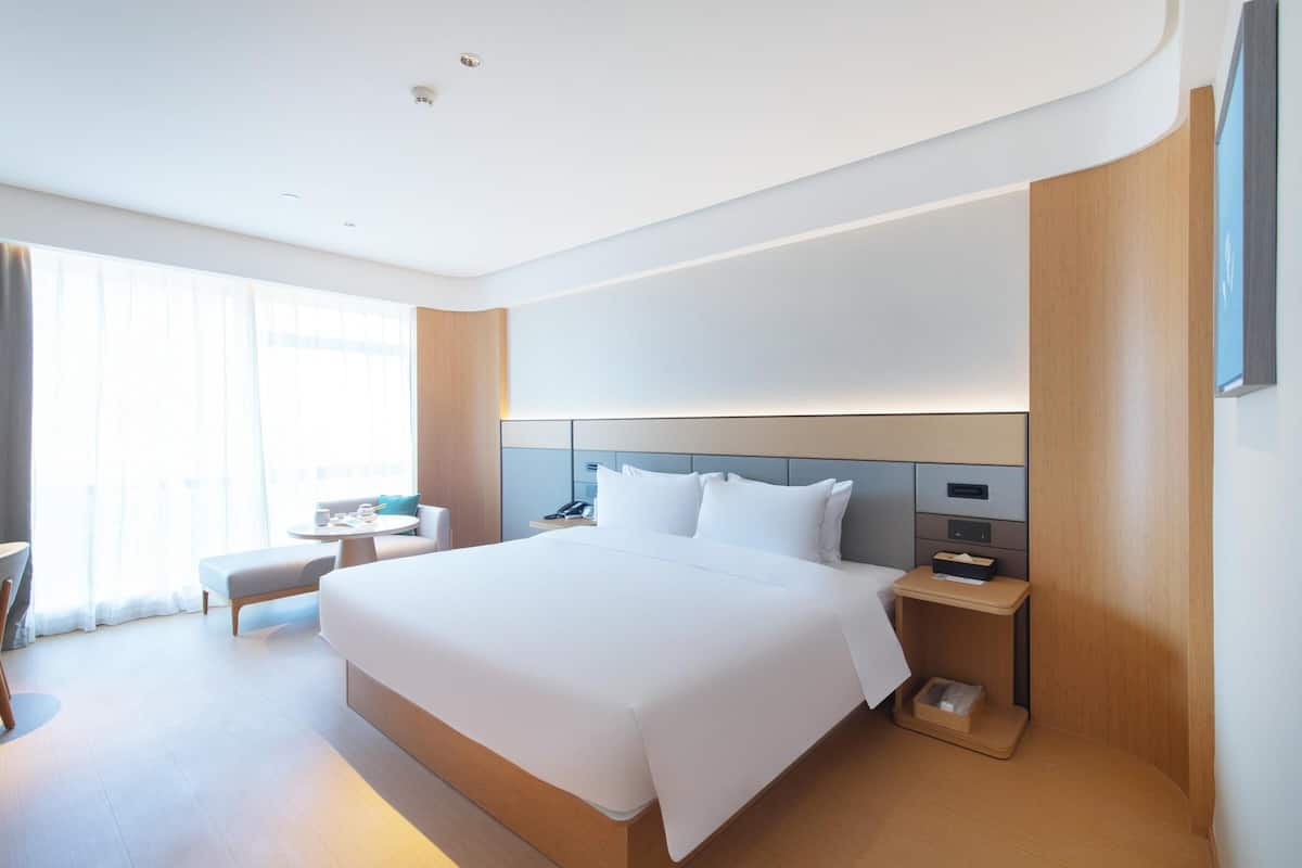 Et moderne hotelværelse med en stor seng, sengeborde, et lille siddeområde og et stort vindue.