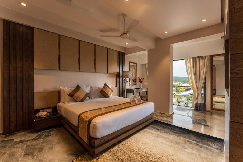 A modern hotel room with a large bed, a ceiling fan, a desk with a lamp, and a view of the outdoors.