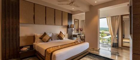 A modern hotel room with a large bed, a ceiling fan, a desk with a lamp, and a view of the outdoors.