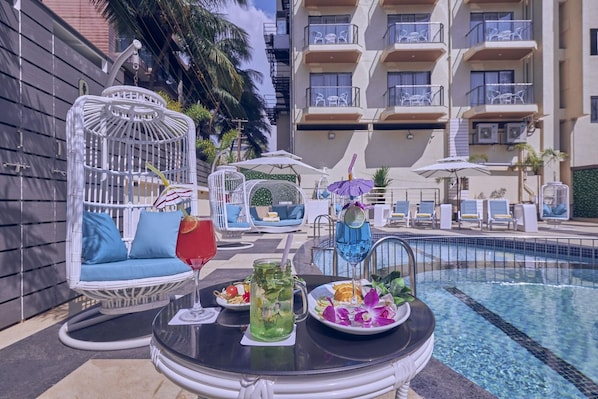 A poolside area with lounge chairs, a dining table with a drink, and a pool. - Regenta Central Imperial Candolim (Candolim)