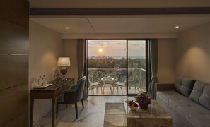 A modern hotel room with a balcony, a desk with a lamp, a sofa, and a view of the ocean at sunset. - Regenta Central Imperial Candolim (Candolim)