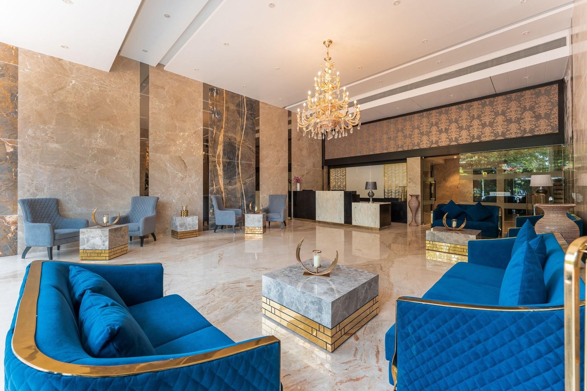 A spacious lobby with marble flooring, a grand chandelier, and blue upholstered seating.