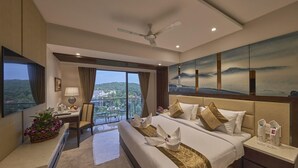 A hotel room with a bed, a desk, a chair, a balcony with a view, and a ceiling fan. - Regenta Central Imperial Candolim (Candolim)