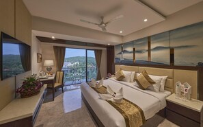 A hotel room with a bed, a desk, a chair, a balcony with a view, and a ceiling fan. - Regenta Central Imperial Candolim (Candolim)