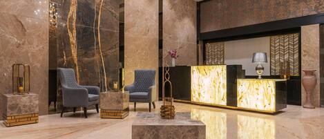 A lobby with marble walls, two blue upholstered chairs, a reception desk, and a chandelier.
