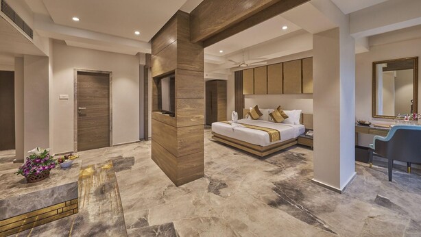 A modern hotel room with a large bed, a vanity with a mirror, and a seating area with a table. - Regenta Central Imperial Candolim (Candolim)