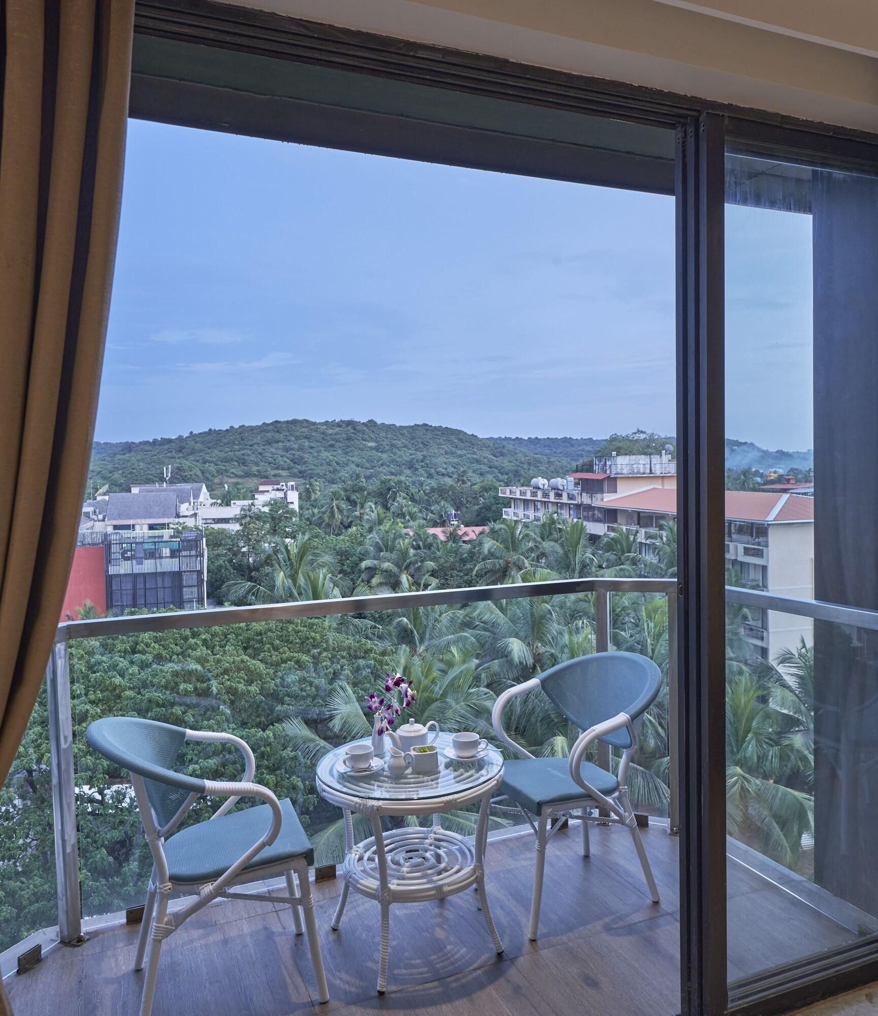 A balcony with a table and chairs, overlooking a cityscape with buildings and greenery.