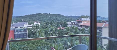 A balcony with a table and chairs, overlooking a cityscape with buildings and greenery.