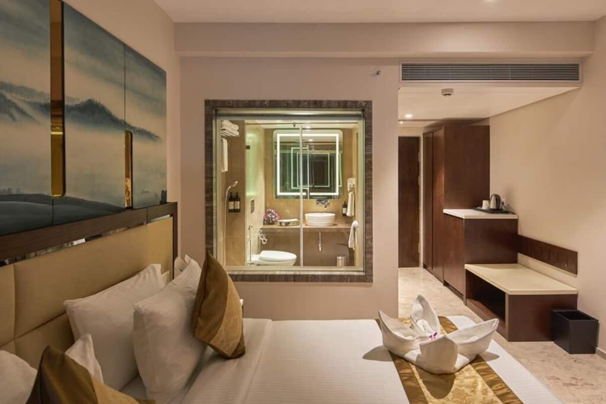 A hotel room with a large bed, a bathroom with a glass-enclosed shower, and a view of the mountains.