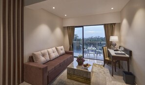 A modern living room with a sofa, a coffee table, a desk with a lamp, and a balcony with a table and chairs. - Regenta Central Imperial Candolim (Candolim)