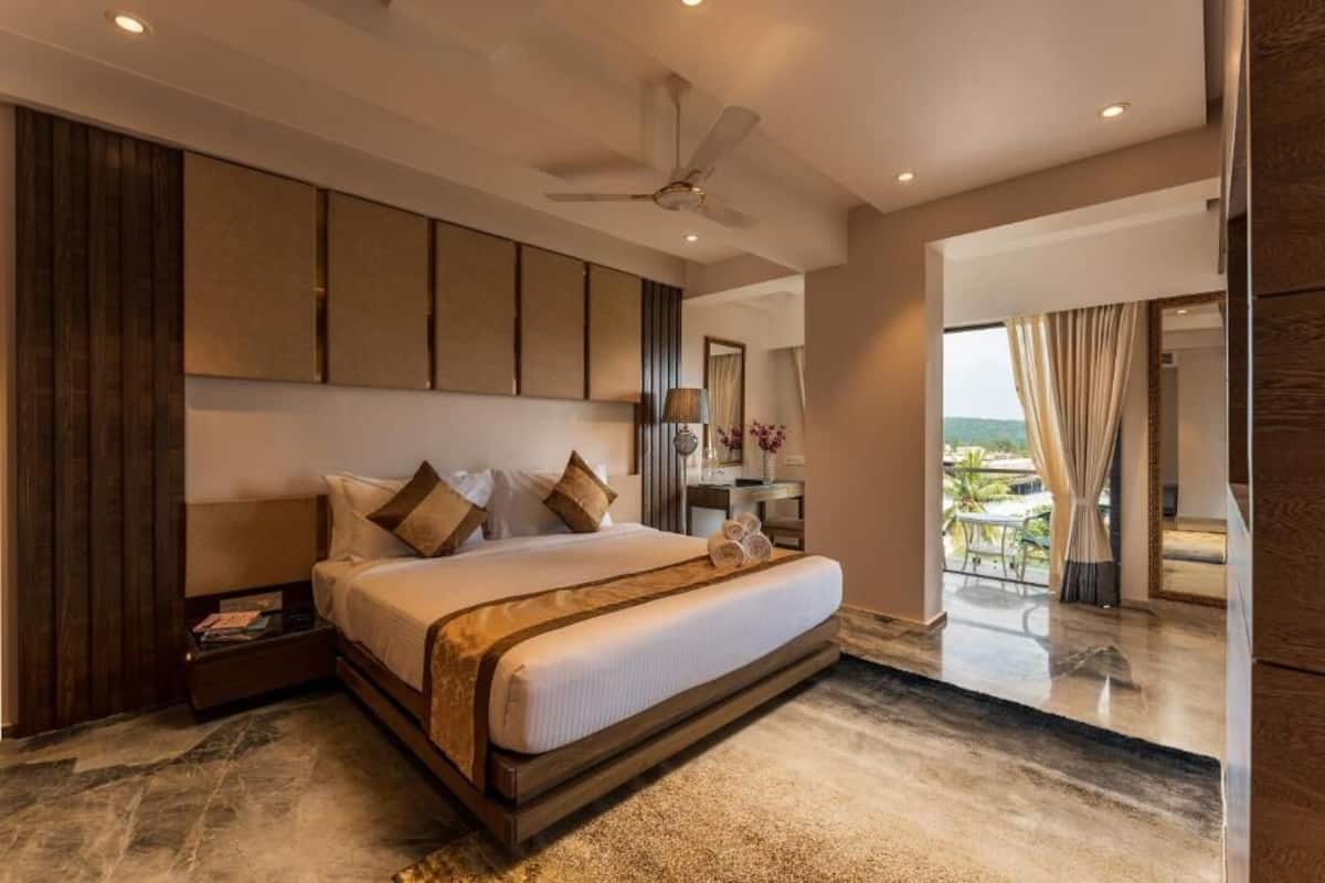 A modern hotel room with a large bed, a ceiling fan, a desk with a lamp, and a view of the outdoors.