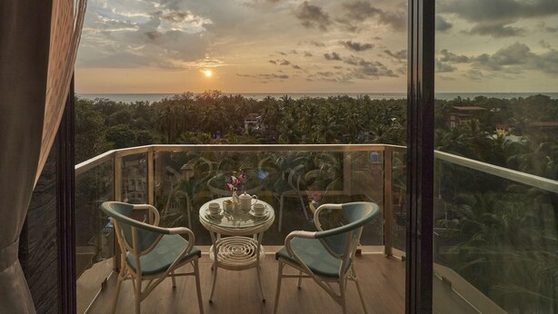 A balcony with two chairs and a table, overlooking a cityscape and palm trees. - Regenta Central Imperial Candolim (Candolim)