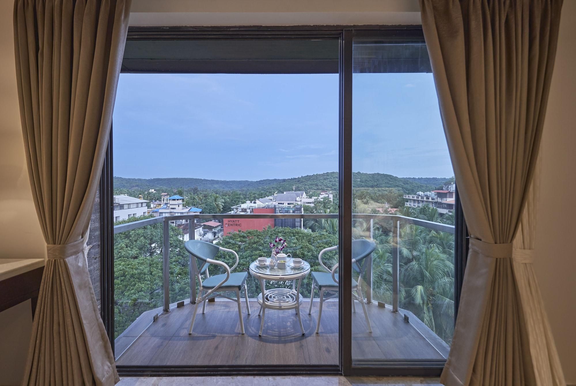 A balcony with a table and chairs, overlooking a cityscape and greenery.
