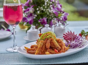A table setting with a plate of fried food, a glass of pink beverage, and a floral arrangement. - Regenta Central Imperial Candolim (Candolim)