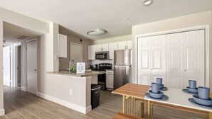 Una cocina moderna con armarios blancos, electrodomésticos de acero inoxidable y una mesa de comedor de madera con vajilla azul.