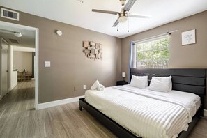 Ein Schlafzimmer mit Bett, Deckenventilator, Fenster mit Jalousien und einem Wandbild.