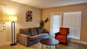 Un salon comprenant un canapé, un fauteuil, une lampe de table et une lampe sur pied, ainsi qu’une œuvre d’art murale.