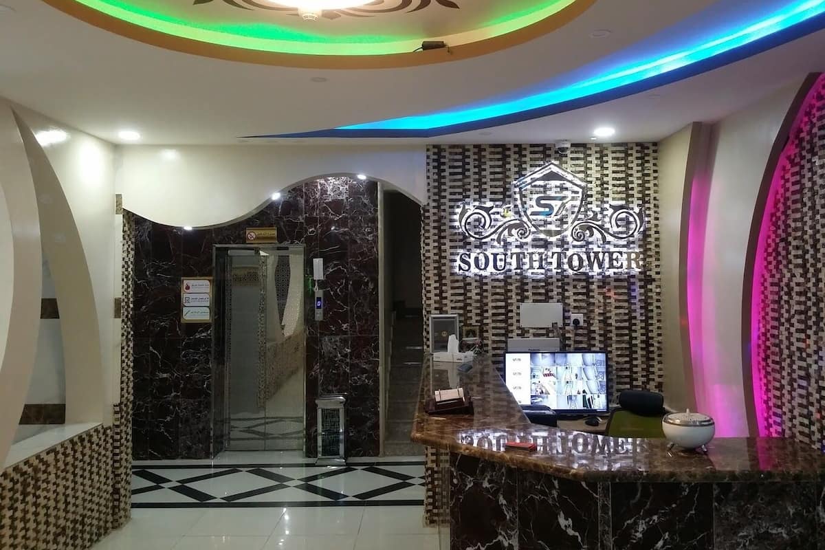 A hotel reception area with a marble reception desk, a digital screen displaying images, and a sign reading "SOUTH TOWER".