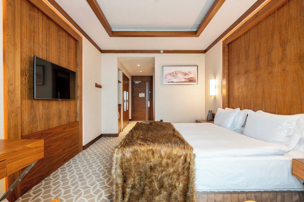 Ein Hotelzimmer mit einem großen Bett, einem flachbildfernseher an der Wand, einem Holzkopfteil und einem gerahmten Bild.