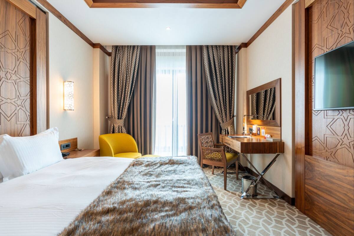 Ein Hotelzimmer mit Bett, Schreibtisch, Stuhl, Fernseher und Vorhängen.