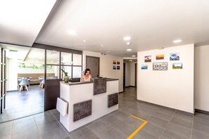A reception area with a receptionist, a seating area with tables and chairs, and a wall with framed pictures. - Hotel Le Virevent (Saint-Raphael)