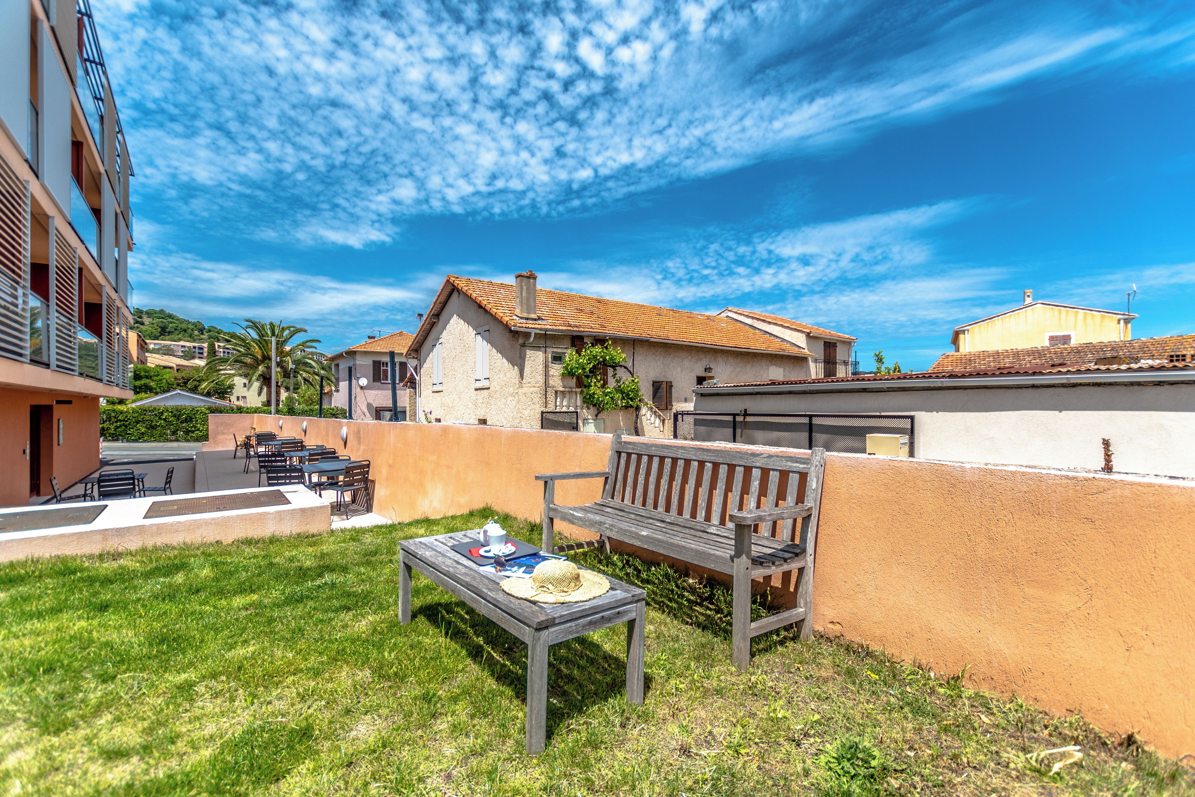 A patio with a wooden table and bench, surrounded by a low wall and a grassy area.
