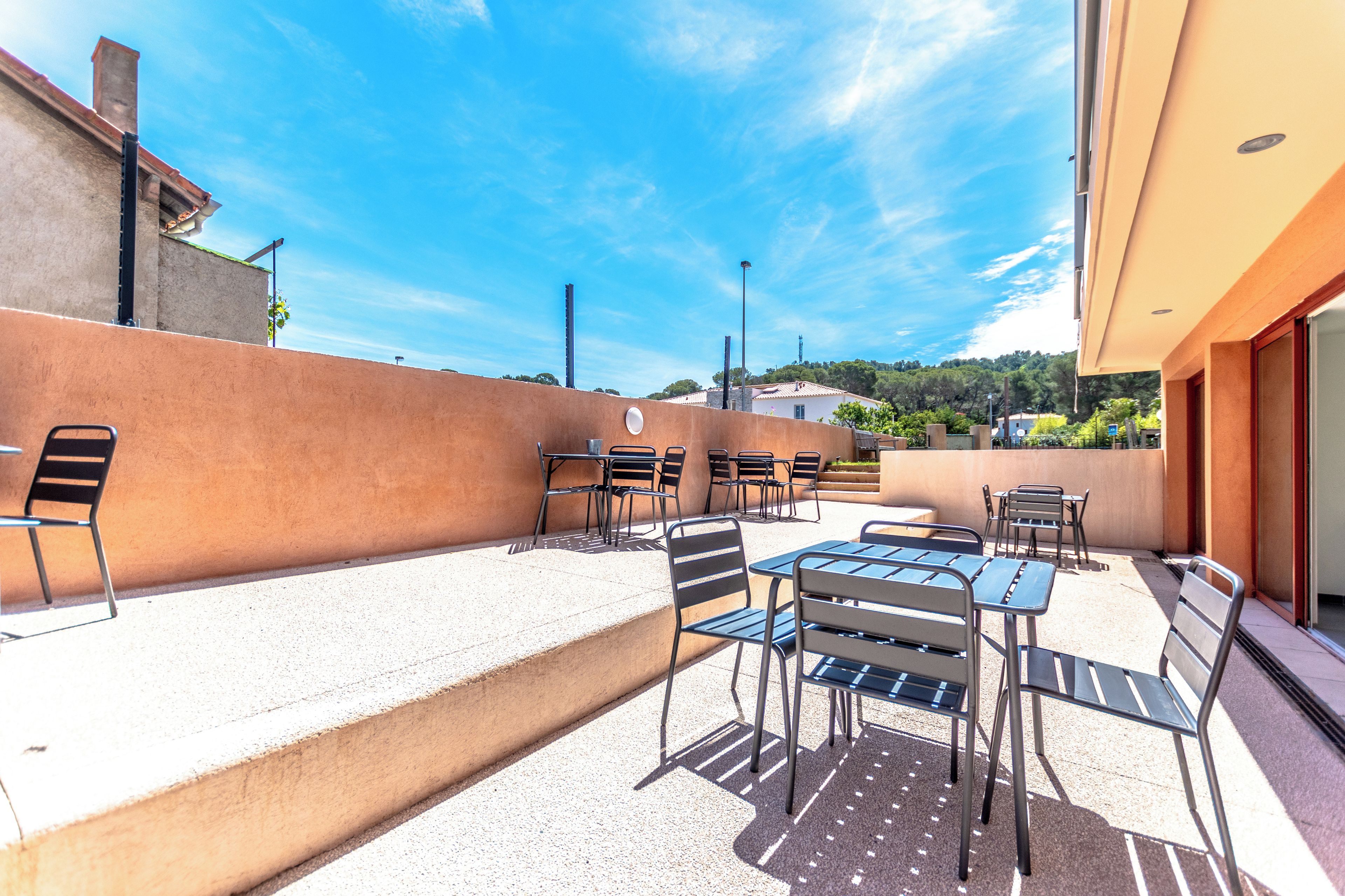 An outdoor patio with metal tables and chairs, a concrete ledge, and a clear blue sky.