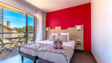Hotellihuone, jossa on suuri sänky, punaisella värillä korostettu seinä ja näkymä rakennukseen suuren ikkunan kautta.