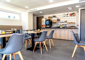 A modern cafe with wooden tables and chairs, a coffee machine, and a counter with snacks and condiments. - Hotel Le Virevent (Saint-Raphael)