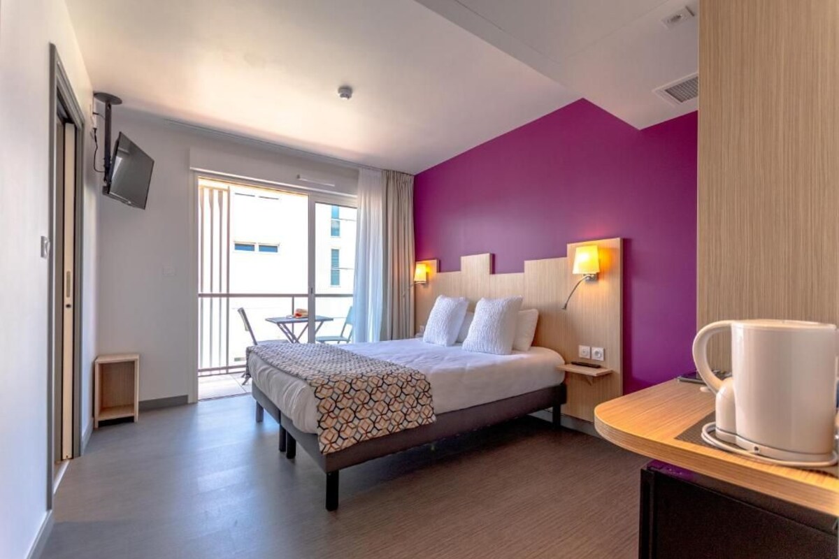 Een hotelkamer met een bed, nachtkastjes, een koffiezetapparaat, een televisie en een balkon met een tafel en stoelen.