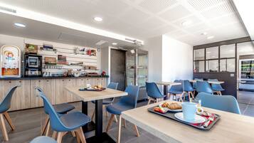 A modern cafe with tables and chairs, a counter with food items, and a coffee machine.