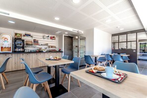 A modern cafe with tables and chairs, a counter with food items, and a coffee machine. - Hotel Le Virevent (Saint-Raphael)
