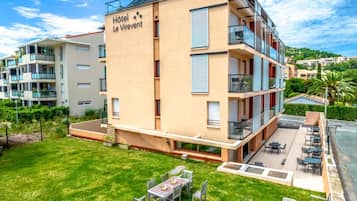 A multi-story hotel building with balconies, a patio area with tables and chairs, and a well-maintained lawn.