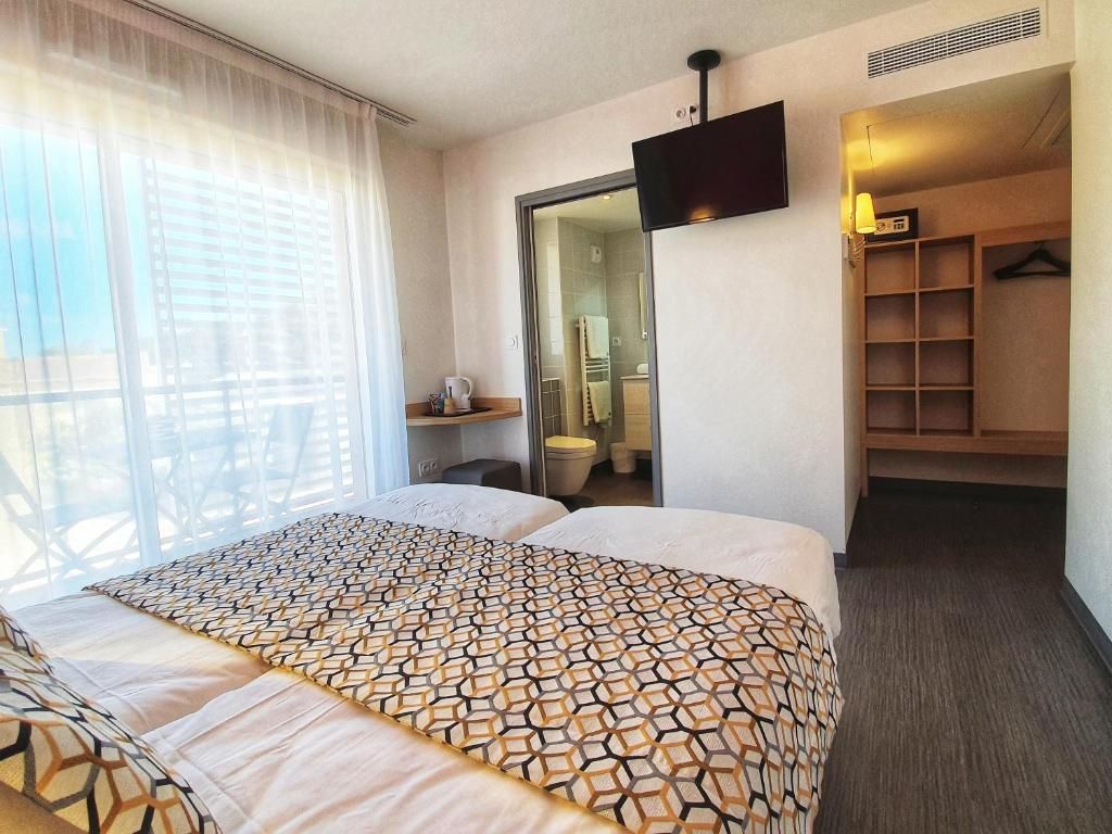 Une chambre d’hôtel avec un grand lit, un téléviseur fixé au mur, un dressing et une salle de bain visible à travers une porte ouverte.