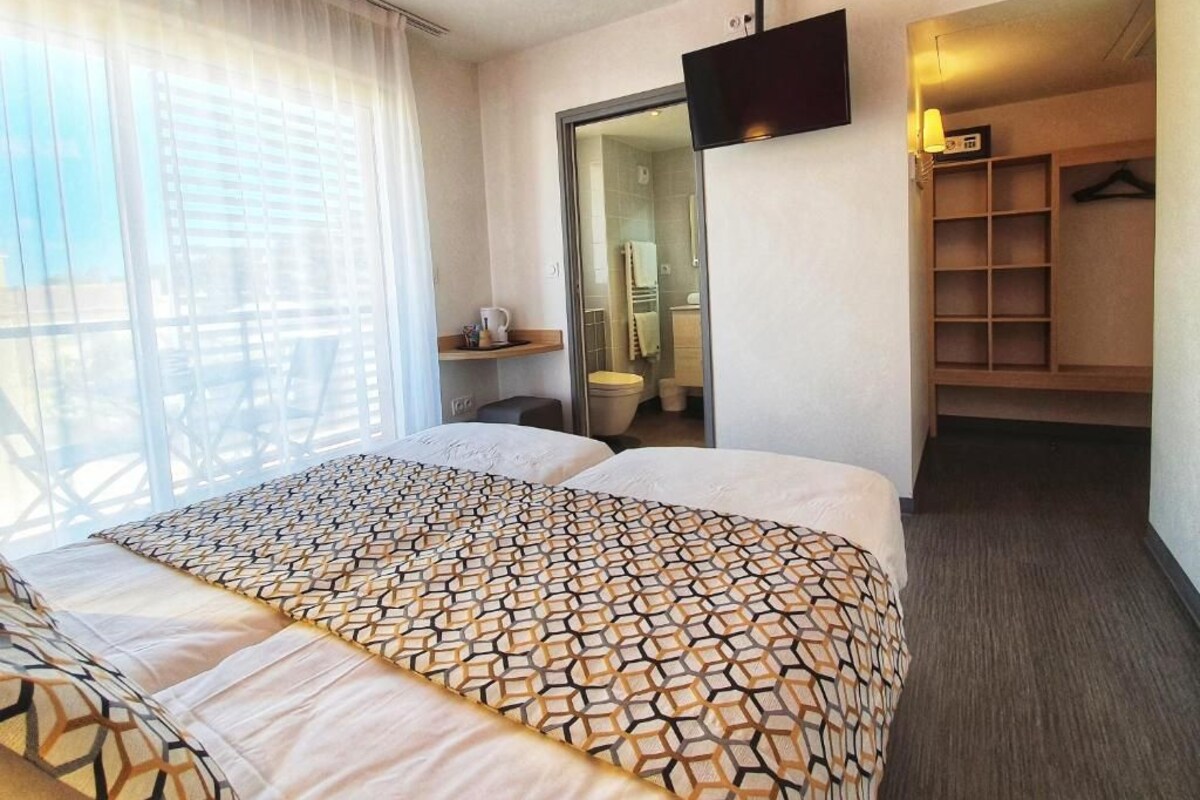 A hotel room with a large bed, a TV mounted on the wall, a walk-in closet, and a bathroom visible through an open door.